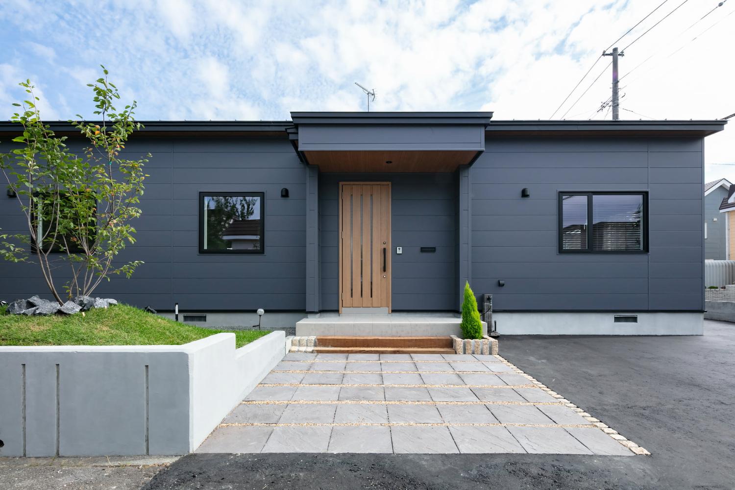シンプルなグレーの外壁に木目の玄関ドアが映える平屋