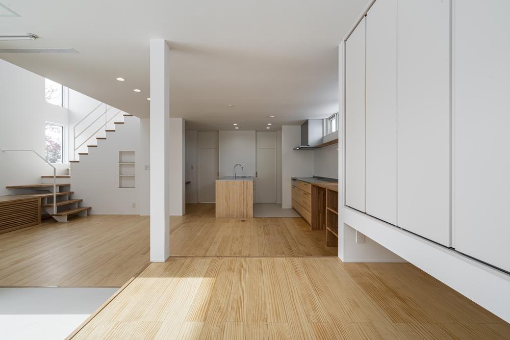 白を基調とした室内に木目の床が広がる、階段とキッチンを備えた開放的な住空間の内観