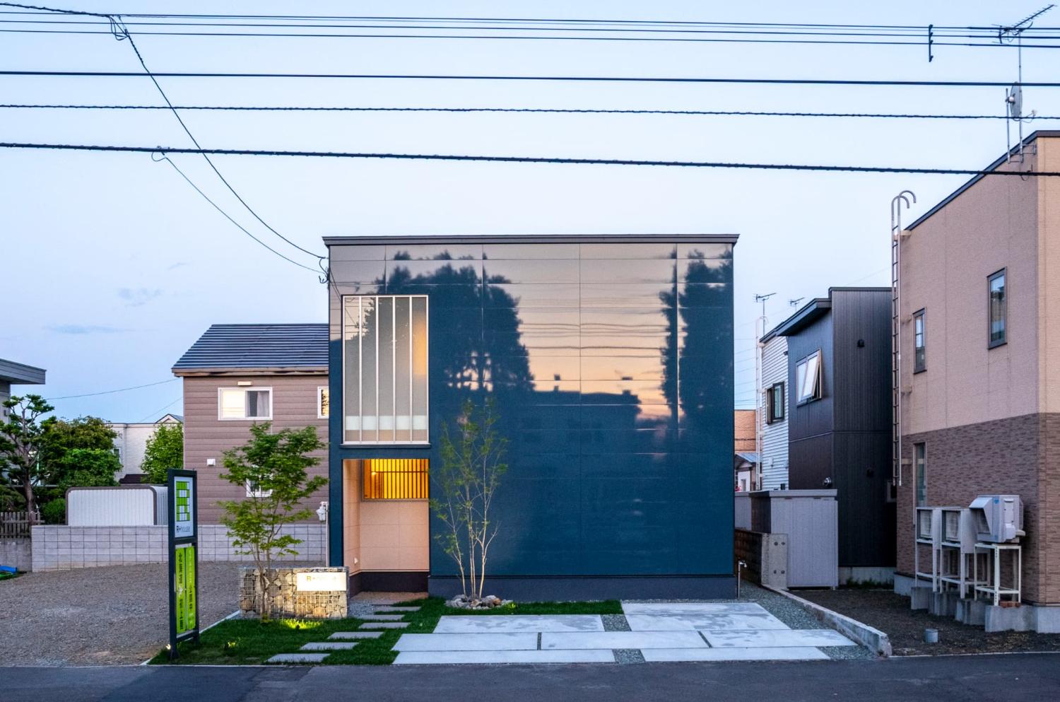 大判の天然石タイルを敷いたアプローチに、芝生と樹木のグリーンを掛け合わせた玄関外構